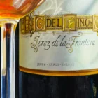 Close-up of a glass of sherry and a bottle of Cayetano del Pino Palo Cortado Solera, showcasing detailed reflections and rich amber tones.