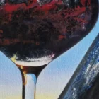 Close-up of a glass of red wine, showing deep red hues and intricate reflections of the sunset within the glass.