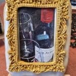 A golden-framed cookie showing a wine glass with bottles in the background.