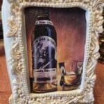 A cream-framed cookie featuring a whiskey bottle and glass against a warm background.