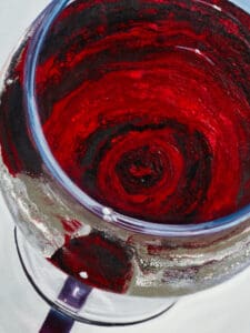 Close-up of crimson wine swirling in a glass with fine textures and light reflections.