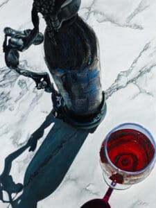 A wine bottle, sculpture, and glass of crimson wine casting shadows on marble.