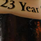 A close-up of the 23 Year Old label on a Pappy Van Winkle bottle, accentuating the textures and golden hues of the painting’s rich details.